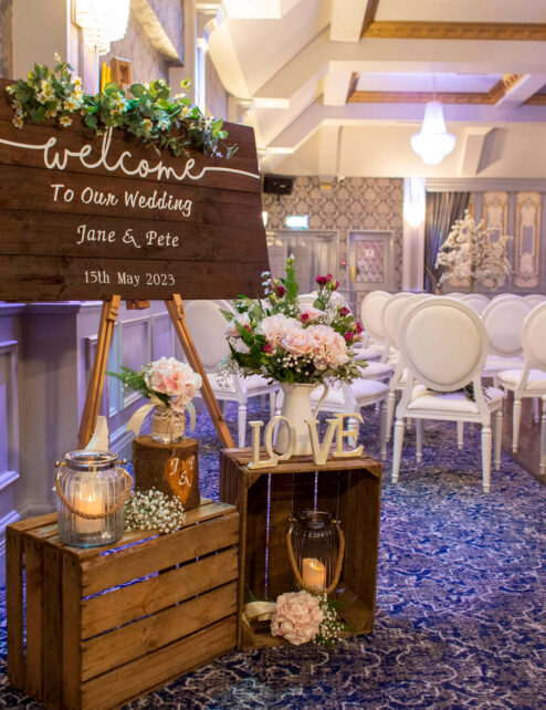 Elegant wedding setup at hotel with floral decor and wooden welcome sign.