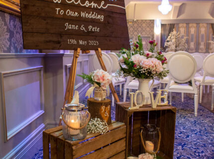 Wedding welcome sign with floral decor in a cosy hotel setting.