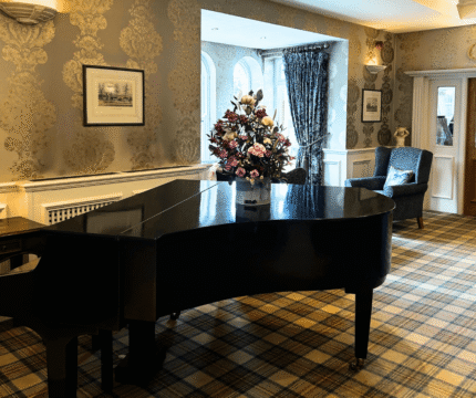 Cosy hotel lounge with piano and floral centrepiece.