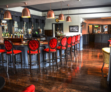 Elegant hotel bar with red seating and copper lights, inviting for social gatherings.