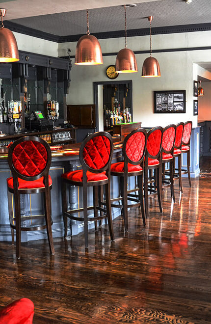 Elegant hotel bar with red seating and copper lights, inviting for social gatherings.
