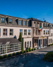 Elegant hotel exterior with Irish flag, car park, welcoming entrance and lush greenery.