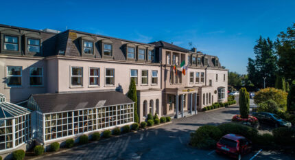 Elegant hotel exterior with Irish flag, car park, welcoming entrance and lush greenery.