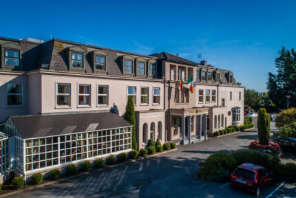 Elegant hotel exterior with Irish flag, car park, welcoming entrance and lush greenery.