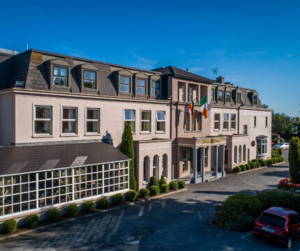 Elegant hotel exterior with Irish flag, car park, welcoming entrance and lush greenery.