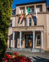 Front entrance of The Anner Hotel with flags and vibrant flower bed.