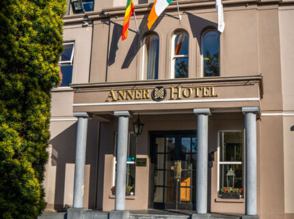 Front entrance of The Anner Hotel with flags and vibrant flower bed.