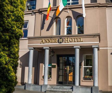Front entrance of The Anner Hotel with flags and vibrant flower bed.