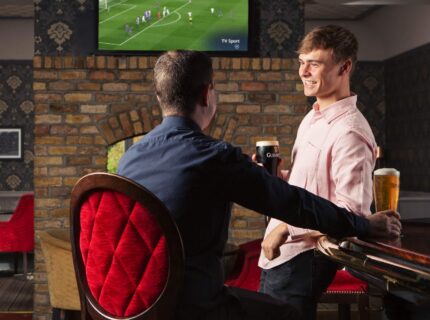 Two friends enjoying drinks and a football match in a cosy hotel bar.