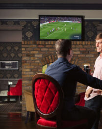 Two friends enjoying drinks at The Anner Hotel bar watching a football match.