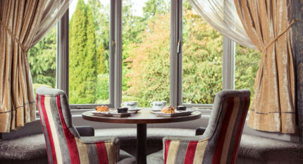 Cosy seating with coffee and pastries by a window overlooking lush greenery.