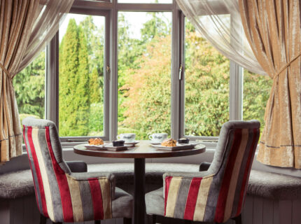 Cosy seating with coffee and pastries by a window overlooking lush greenery.