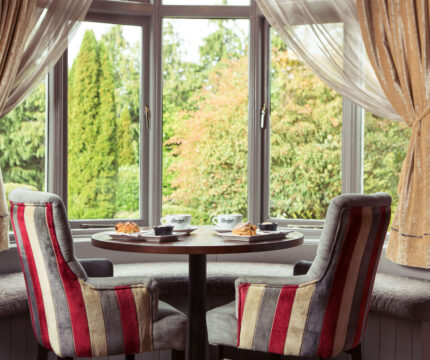 Cosy seating with coffee and pastries by a window overlooking lush greenery.