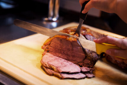 A close-up of a roast beef being carved on a wooden board, showcasing juicy slices.