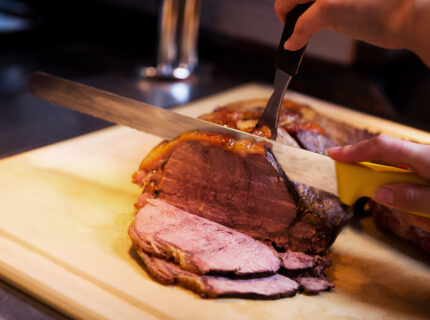A close-up of a roast beef being carved on a wooden board, showcasing juicy slices.