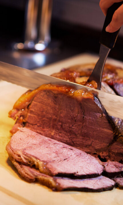 A close-up of a roast beef being carved on a wooden board, showcasing juicy slices.