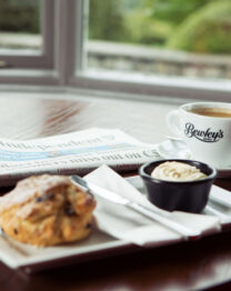 Cosy hotel lounge with coffee, scone, newspaper on table by window.