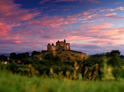 A picturesque historic castle on a hill during a vibrant sunset, surrounded by lush greenery.