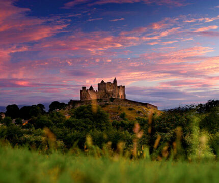 A picturesque historic castle on a hill during a vibrant sunset, surrounded by lush greenery.