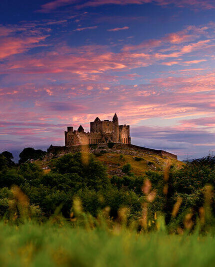 A picturesque historic castle on a hill during a vibrant sunset, surrounded by lush greenery.