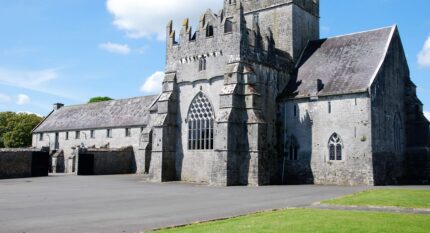 Family exploring historic stone castle with lush green grounds and clear blue sky.