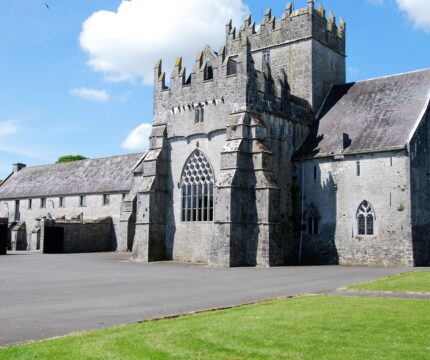 Family exploring historic stone castle with lush green grounds and clear blue sky.