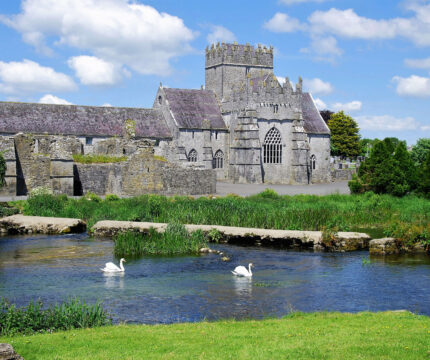 Family enjoying scenic view near historic stone hotel with swans on a tranquil river.