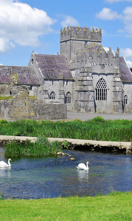 Family enjoying scenic view near historic stone hotel with swans on a tranquil river.