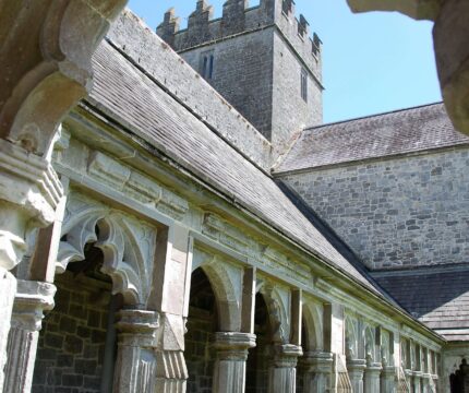 Historic stone cloister with pointed arches at The Anner Hotel, under a clear blue sky.