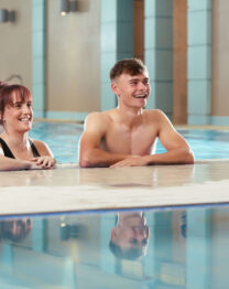 Couple enjoying a relaxing swim at The Anner Hotel's indoor pool, smiling by the edge.