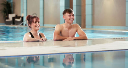 Couple enjoying a relaxing swim at The Anner Hotel's indoor pool, smiling by the edge.