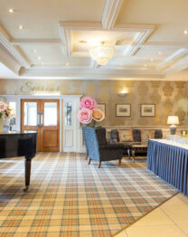 Spacious hotel lobby with elegant decor, grand piano, and drinks table setup.
