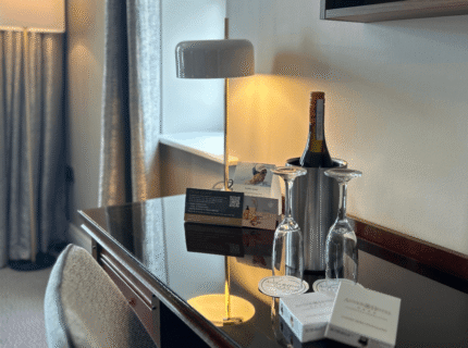 Elegant hotel room with wine, desk, and warm lighting for leisure or work.
