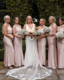 A joyful bridal party in a garden at The Anner Hotel, wearing soft pink dresses.