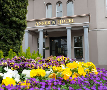 Vibrant flowers in front of The Anner Hotel entrance, inviting and elegant setting.