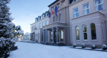 A family enjoys the snowy entrance of The Anner Hotel, decorated with welcoming flags.