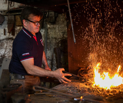 Blacksmith working with fire and tools in a rustic forge setting.