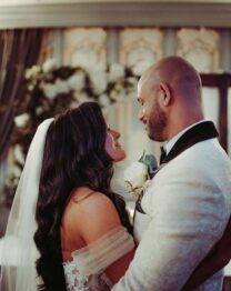 Couple embracing in elegant hotel ballroom with floral backdrop.