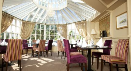 Elegant dining area with striped chairs under a glass ceiling at The Anner Hotel.
