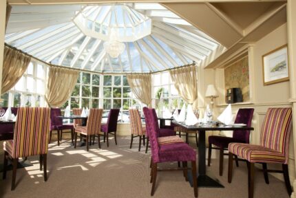Elegant dining area with striped chairs under a glass ceiling at The Anner Hotel.