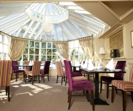 Elegant dining area with striped chairs under a glass ceiling at The Anner Hotel.