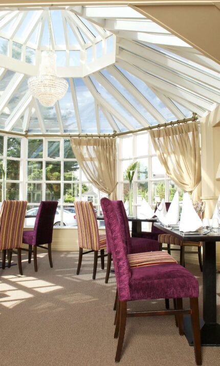 Elegant dining area with striped chairs under a glass ceiling at The Anner Hotel.