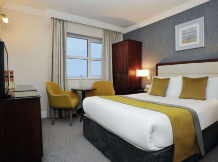 Cosy hotel room with a large bed, mustard chairs, and a view. Ideal for family stays.