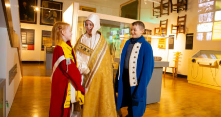 Children in historical costumes enjoy an interactive museum exhibit in a cosy setting.
