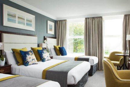 Elegant hotel room with three neatly made beds, plush cushions, and large windows.