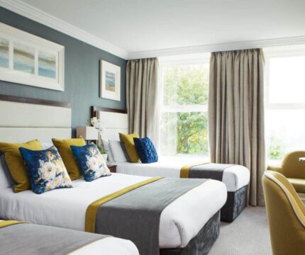 Bright hotel room with three cosy beds, plush pillows, and a view of lush greenery.