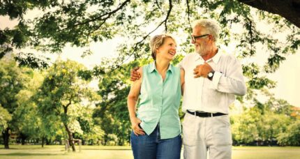 A joyful couple strolls arm-in-arm in a sunny, lush garden at The Anner Hotel.
