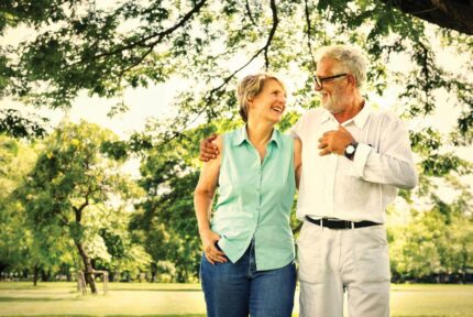 A joyful couple strolls arm-in-arm in a sunny, lush garden at The Anner Hotel.