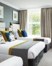 Elegant hotel room with three cosy beds, plush seating, and large window views.