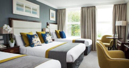 Elegant hotel room with three cosy beds, plush seating, and large window views.